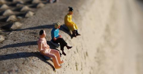 Three scale model people sitting on a street curb.