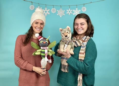 One adult holding a firefly puppet, another adult holding a wolf puppet against a blue backdrop.