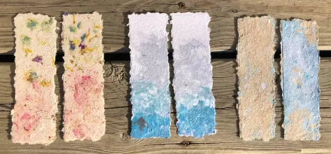 3 sets of 2 bookmarks, each with rough deckled edges. The pair on the left is a pale yellow with green and pink botanical inclusions, the pair in the middle are a pale gray to blue gradient, and the pair on the right area beige and blue.