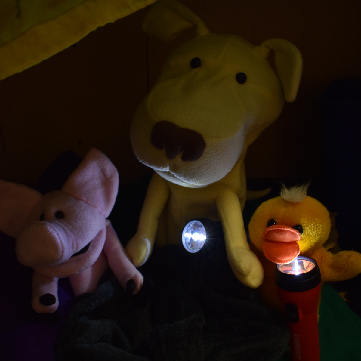 The puppets Joxter the Pig, George the Dog, and Mr. Ducky with flashlights in a blanket fort