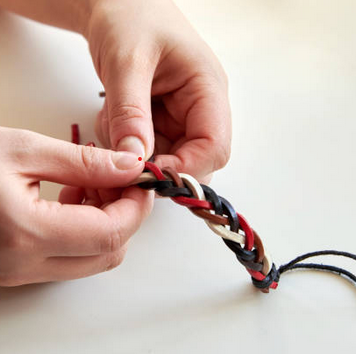 Two hands braiding multicolored cords in front of a white background